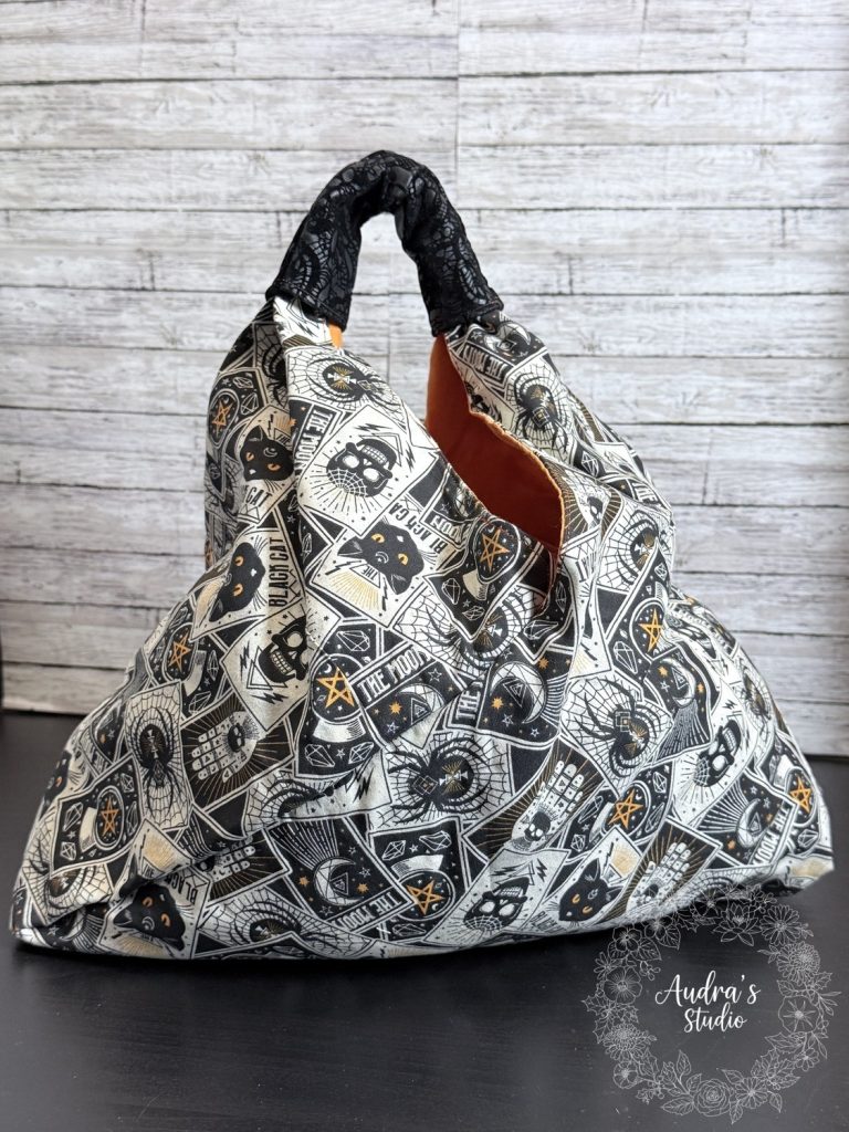 Handmade fabric knot bag in a black and cream tarot card print with black cats and moons, orange lining showing at the opening